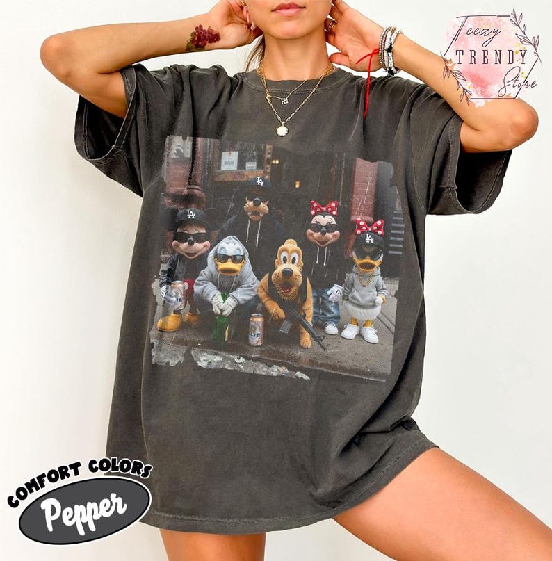 May include: A charcoal gray short-sleeve t-shirt featuring a graphic print of cartoon characters wearing baseball caps and casual clothing. The design includes Mickey Mouse, Donald Duck, Goofy, Pluto, and Minnie Mouse in a street-style setting.