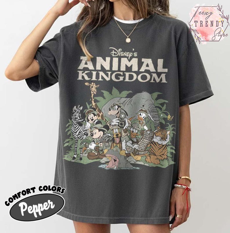 May include: Dark grey t-shirt with the text "Disney's Animal Kingdom" and a graphic of Disney characters such as Mickey Mouse, Donald Duck, and Goofy, alongside a zebra, giraffe, and tiger. The shirt has a Comfort Colors Pepper label.