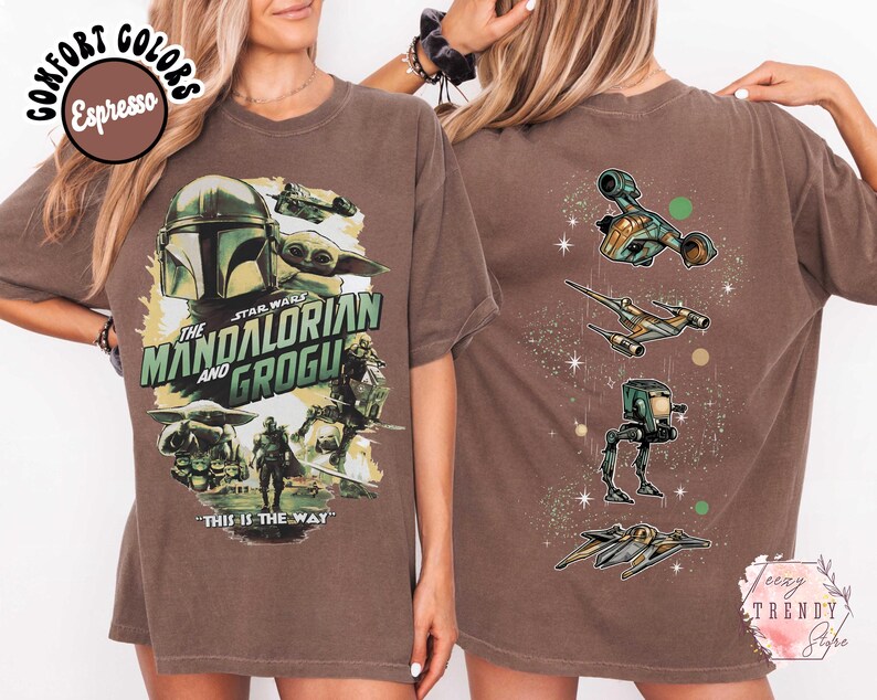 K&ouml;nnte beinhalten: Ein espresso-braunes T-Shirt mit einem Grafikdruck von The Mandalorian und Grogu auf der Vorderseite, inklusive des Textes "The Mandalorian and Grogu" und "This is the way". Die R&uuml;ckseite zeigt eine vertikale Anordnung von vier Star Wars Fahrzeugen.