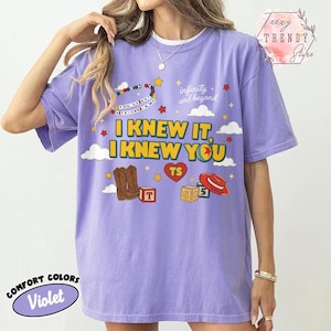 Puede incluir: Una camiseta violeta de manga corta con un estampado gr&aacute;fico que incluye el texto "I KNEW IT, I KNEW YOU", "infinity and beyond" y "YOU'VE GOT A FRIEND IN ME". El dise&ntilde;o muestra ilustraciones de botas vaqueras, un sombrero rojo, bloques y estrellas.