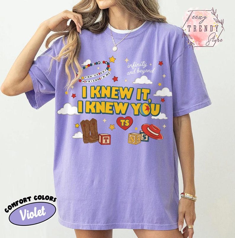 Puede incluir: Una camiseta violeta de manga corta con un estampado gr&aacute;fico que incluye el texto "I KNEW IT, I KNEW YOU", "infinity and beyond" y "YOU'VE GOT A FRIEND IN ME". El dise&ntilde;o muestra ilustraciones de botas vaqueras, un sombrero rojo, bloques y estrellas.