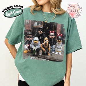 May include: A light green t-shirt featuring a graphic print of cartoon characters wearing sunglasses and streetwear, including hats and hoodies. The text COMFORT COLORS Light Green appears in the top left, and the text Teezy TRENDY Store is in the top right.