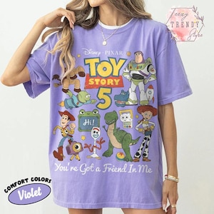May include: A violet short-sleeve t-shirt featuring a graphic print of Disney Pixar Toy Story characters including Woody, Buzz Lightyear, Jessie, Rex, and Forky. The text reads Toy Story 5 and You've Got a Friend In Me, with a small Hi sign.