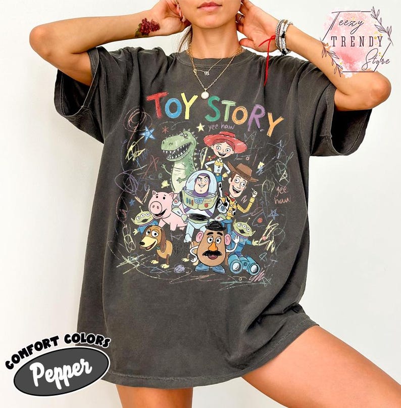May include: Dark grey t-shirt featuring the words "Toy Story" in colorful letters, with a graphic of characters from the movie. The shirt has a vintage look with the words "Comfort Colors" and "Pepper" printed on the bottom.