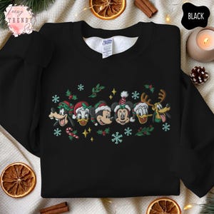 May include: Black sweatshirt featuring embroidered Disney characters in Christmas hats. The design includes Mickey Mouse, Minnie Mouse, Donald Duck, Goofy, and Pluto, with snowflakes and candy canes. The sweatshirt has a crew neck.