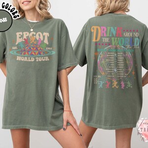 May include: Moss green t-shirt with front and back graphics. The front graphic says "EPCOT World Tour" with a colorful design. The back graphic says "Drink Around The World" with a globe and country names.