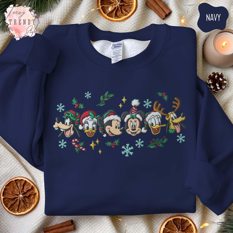 May include: Navy blue sweatshirt featuring embroidered Disney characters in Christmas attire. The design includes Mickey Mouse, Minnie Mouse, Donald Duck, Goofy, and Pluto, with snowflakes and festive accents. The sweatshirt is a cozy, seasonal apparel item.
