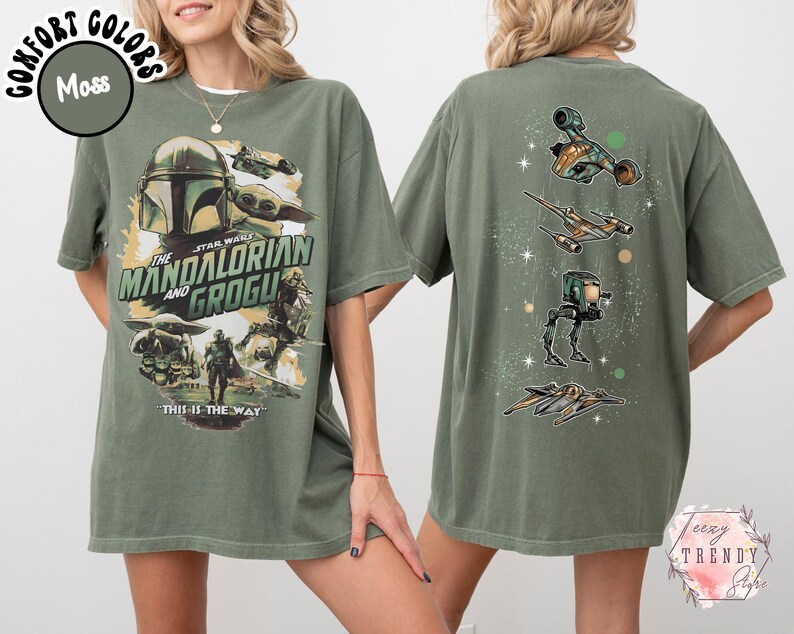 K&ouml;nnte beinhalten: Ein moosgr&uuml;nes T-Shirt mit einer Grafik auf der Vorderseite von The Mandalorian und Grogu sowie dem Text "The Mandalorian and Grogu" und "This is the way". Die R&uuml;ckseite zeigt eine vertikale Anordnung von vier Star Wars Raumfahrzeugen.