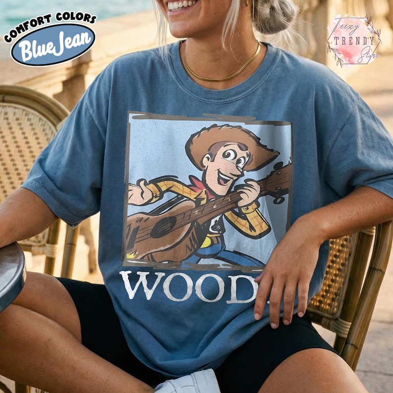 May include: Blue t-shirt featuring a cartoon cowboy playing a guitar, with the word "WOOD" beneath. The shirt has the words "Comfort Colors" and "Blue Jean" in a circular design on the upper left.