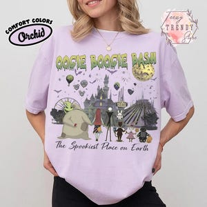 May include: A light purple t-shirt featuring a graphic print with the text OOGIE BOOGIE BASH and The Spookiest Place on Earth. The design includes characters from The Nightmare Before Christmas, a castle, a moon, and various park attractions.