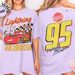 May include: Light purple t-shirt featuring a graphic of Lightning McQueen from the Cars movie. The front design includes the number 95, the character's name, and a checkered flag. The back displays a large yellow 95 and the Lightning McQueen logo.