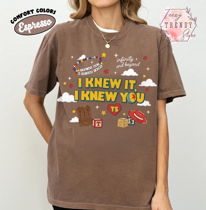 Puede incluir: Una camiseta de manga corta color marr&oacute;n espresso con un estampado gr&aacute;fico que incluye el texto I KNEW IT, I KNEW YOU, infinity and beyond y YOU'VE GOT A FRIEND IN ME. El dise&ntilde;o incluye una pulsera de cuentas, botas vaqueras, bloques y un sombrero rojo.