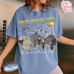 May include: A blue jean colored t-shirt featuring a graphic print with the text OOGIE BOOGIE BASH and The Spookiest Place on Earth. The design includes illustrations of a castle, a moon, and various characters from a movie, set against a background of fireworks, bats, and balloons.