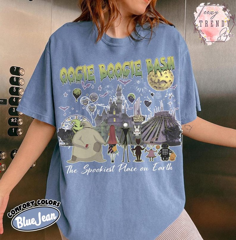 May include: A blue jean colored t-shirt featuring a graphic print with the text OOGIE BOOGIE BASH and The Spookiest Place on Earth. The design includes illustrations of a castle, a moon, and various characters from a movie, set against a background of fireworks, bats, and balloons.