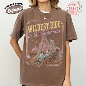 Może przedstawiać: T-shirt w kolorze espresso z grafiką w stylu vintage. Grafika głosi "Wildest Ride in the Wilderness" z pociągiem i postaciami. Koszulka ma okrągły dekolt i kr&oacute;tkie rękawy. Koszulka jest w kolorze komfortowym.