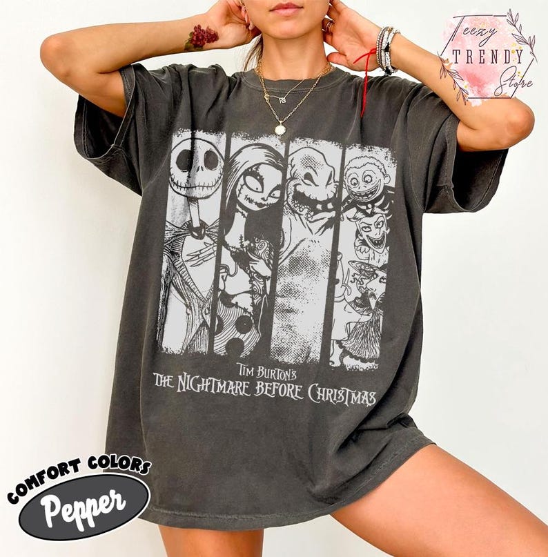 May include: A charcoal grey short-sleeve t-shirt featuring a white graphic print of characters from Tim Burton's The Nightmare Before Christmas. The design is divided into vertical panels showing Jack Skellington, Sally, Oogie Boogie, and Lock, Shock, and Barrel.