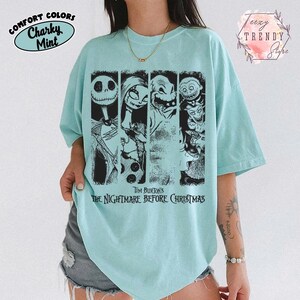 May include: A light mint green short-sleeve t-shirt featuring a black graphic print of characters from Tim Burton's The Nightmare Before Christmas. The design includes four vertical panels showing Jack Skellington, Sally, Oogie Boogie, and Lock, Shock, and Barrel.