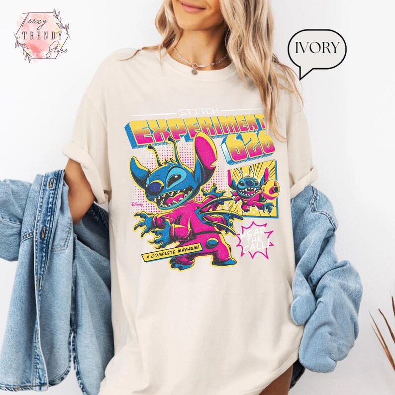 Pode incluir: Camiseta de cor marfim com um gr&aacute;fico colorido de Stitch de Lilo & Stitch. O design inclui o texto "Stitch Experiment 626" e "A Complete Mayhem!" em um estilo retro de banda desenhada. A camiseta tem mangas curtas.