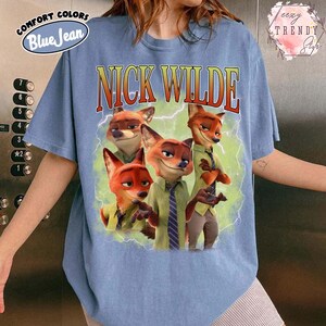 Puede incluir: Camiseta azul claro con un gr&aacute;fico del personaje Nick Wilde de la pel&iacute;cula Zootr&oacute;polis. El gr&aacute;fico incluye el texto "NICK WILDE" en una fuente retro. La camiseta est&aacute; etiquetada como "COMFORT COLORS Blue Jean".