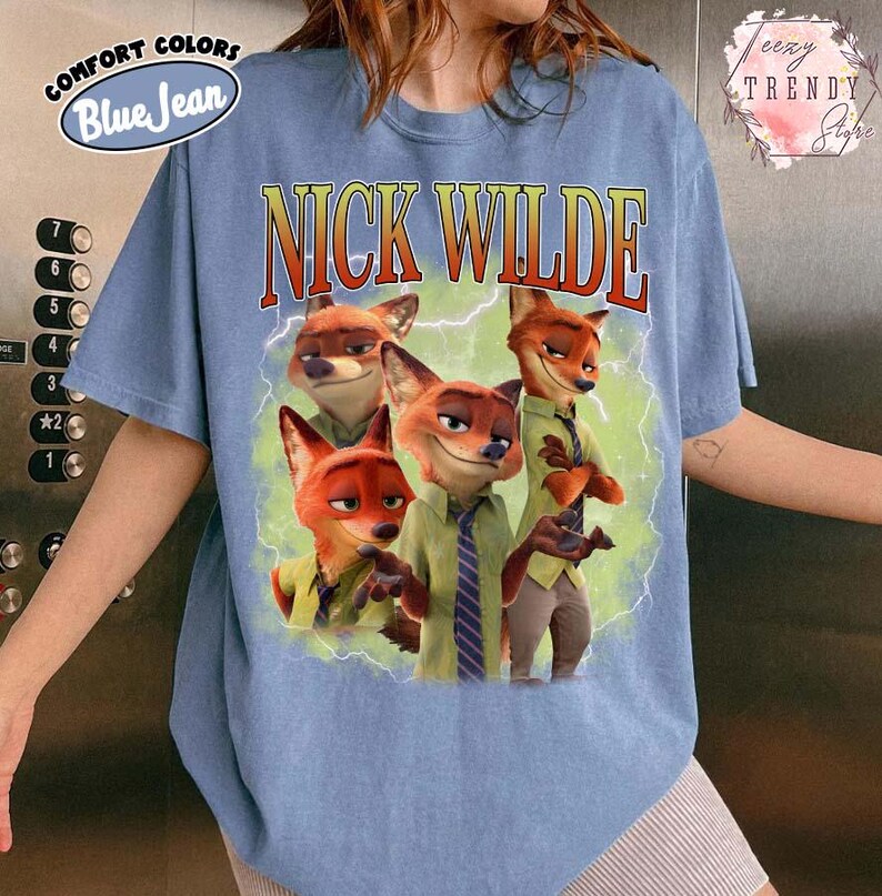 Puede incluir: Camiseta azul claro con un gr&aacute;fico del personaje Nick Wilde de la pel&iacute;cula Zootr&oacute;polis. El gr&aacute;fico incluye el texto "NICK WILDE" en una fuente retro. La camiseta est&aacute; etiquetada como "COMFORT COLORS Blue Jean".