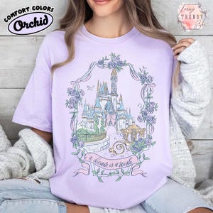 Puede incluir: Camiseta de color lila con una ilustraci&oacute;n de un castillo enmarcada por una corona floral. El dise&ntilde;o incluye un carrusel y una pancarta con el texto "a dream is a wish". La camiseta tambi&eacute;n presenta el logotipo de Comfort Colors. Un estilo casual y c&oacute;modo.