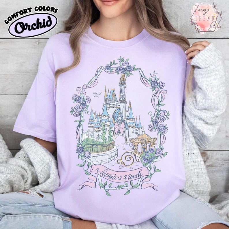 Puede incluir: Camiseta de color lila con una ilustraci&oacute;n de un castillo enmarcada por una corona floral. El dise&ntilde;o incluye un carrusel y una pancarta con el texto "a dream is a wish". La camiseta tambi&eacute;n presenta el logotipo de Comfort Colors. Un estilo casual y c&oacute;modo.