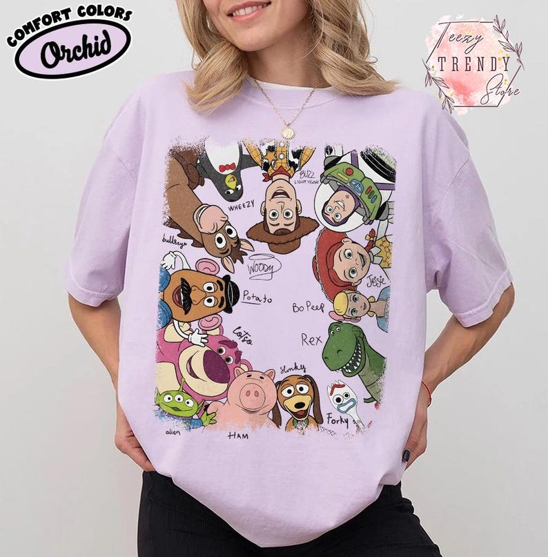 May include: Orchid Comfort Colors t-shirt featuring a colorful graphic of Toy Story characters. The design includes Woody, Buzz Lightyear, Jessie, and others. The shirt also has the text "eezy TRENDY Stighe".