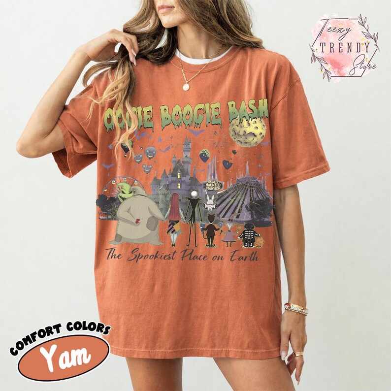 May include: A rust-colored short-sleeve t-shirt featuring a graphic print with the text OOGIE BOOGIE BASH and The Spookiest Place on Earth. The design includes various animated characters, a castle, a moon, and bats in shades of green and purple.