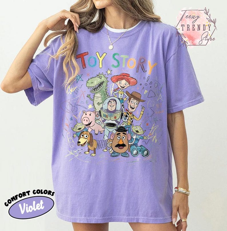 May include: Violet Comfort Colors t-shirt featuring a colorful graphic of Toy Story characters. The design includes Woody, Buzz Lightyear, and other beloved characters from the animated film. The shirt has short sleeves and a relaxed fit.