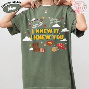 Puede incluir: Una camiseta de manga corta color verde musgo con un estampado gr&aacute;fico que incluye el texto "I KNEW IT, I KNEW YOU", "infinity and beyond" y "YOU'VE GOT A FRIEND IN ME". El dise&ntilde;o muestra botas de vaquero, un sombrero rojo y cubos.