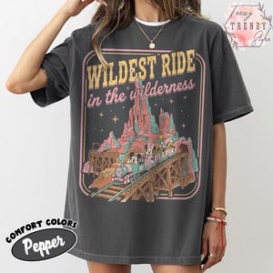 Może przedstawiać: Ciemnoszara koszulka z grafiką w stylu vintage przedstawiającą pociąg z Myszka Miki i Minnie, napisem "Wildest Ride in the Wilderness" oraz słowami "Comfort Colors Pepper."