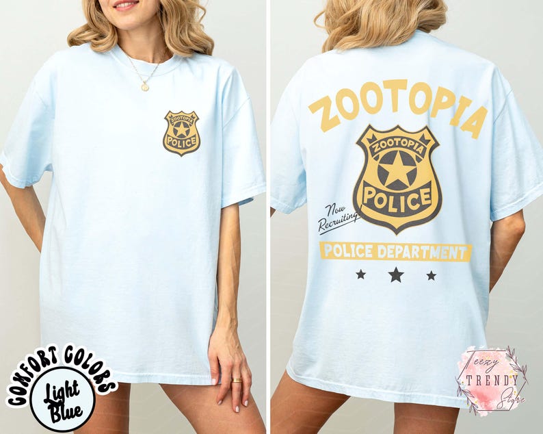 May include: Light blue t-shirt featuring a Zootopia Police badge on the front and back. The back of the shirt displays the words "ZOOTOPIA POLICE DEPARTMENT" in yellow, with "Now Recruiting" text. The shirt has a relaxed fit.