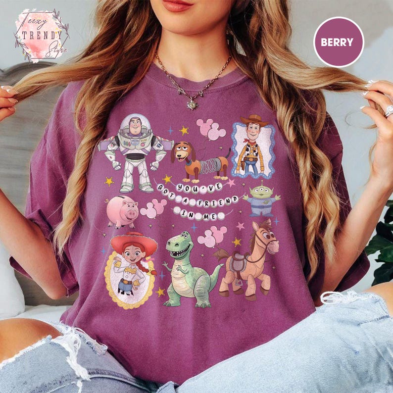 May include: Berry-colored t-shirt featuring a graphic of various Toy Story characters, including Buzz Lightyear, Woody, and others. The phrase "You've Got a Friend in Me" is displayed. The shirt has a relaxed fit.