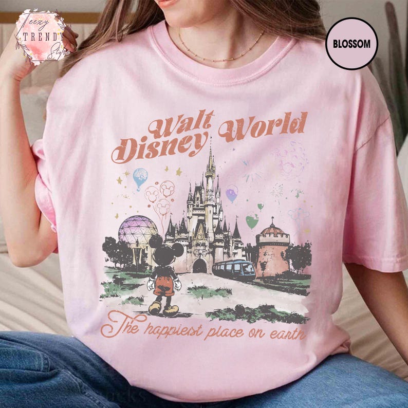 May include: Pink t-shirt with a graphic of Cinderella's castle, Mickey Mouse, and the text "Walt Disney World" and "The happiest place on earth." The shirt has a crew neck and short sleeves.
