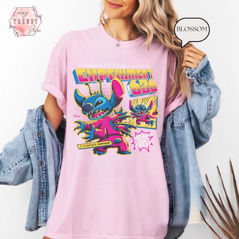 Pode incluir: Camiseta rosa claro com um desenho do Stitch de Lilo & Stitch. O design inclui o texto "Stitch Experiment 626" em estilo retr&ocirc;, com Stitch em uma roupa rosa e azul. O texto adicional diz "A Complete Mayhem!" e "Hear the Call!"