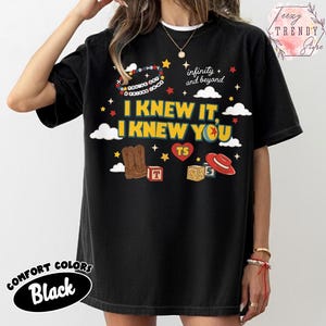 Puede incluir: Una camiseta negra con un estampado gr&aacute;fico que incluye el texto I KNEW IT, I KNEW YOU, infinity and beyond, y YOU'VE GOT A FRIEND IN ME. El dise&ntilde;o presenta ilustraciones de botas vaqueras marrones, un sombrero rojo, bloques, estrellas y nubes.