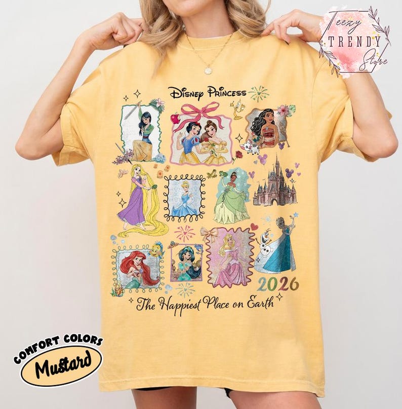 May include: Mustard-colored t-shirt featuring Disney Princesses in framed illustrations. The shirt includes the text "Disney Princess" and "The Happiest Place on Earth" with the year "2026". The shirt is labeled "Comfort Colors".