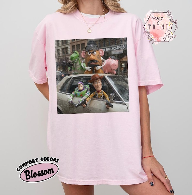 Puede incluir: Una camiseta rosa claro con un estampado gr&aacute;fico de personajes de Toy Story, incluidos Woody, Buzz Lightyear, Rex, Mr. Potato Head y Hamm, colocados dentro y sobre un coche. La camiseta incluye el texto Teezy Trendy Store.