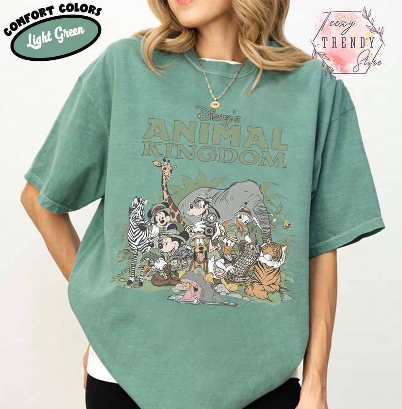 May include: Light green t-shirt with the text "Disney's Animal Kingdom" and a graphic of Disney characters and animals. The shirt has short sleeves and a crew neck. The words "Comfort Colors" and "Light Green" are in a green oval on the top left.