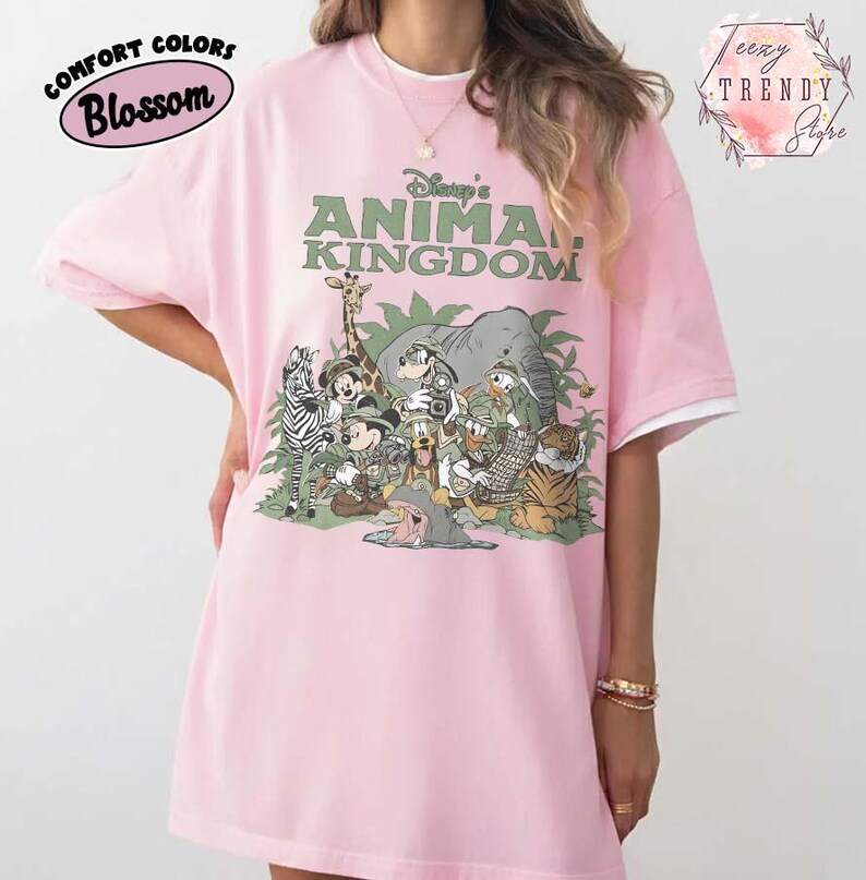 May include: Pale pink t-shirt with the text "Disney's Animal Kingdom" in green. The shirt features a graphic of cartoon animals, including a zebra, giraffe, elephant, and tiger. The sleeves have white trim.