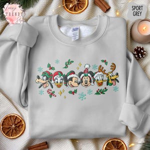 May include: Sport grey sweatshirt featuring embroidered Disney characters in Christmas hats. The design includes Goofy, Donald Duck, Mickey Mouse, Minnie Mouse, and Pluto, with snowflakes and holly accents. The sweatshirt has a crew neck.