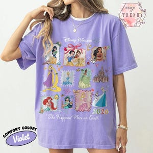 May include: A violet Comfort Colors t-shirt featuring Disney Princesses in framed illustrations. The shirt has the text "Disney Princess", "2026", and "The Happiest Place on Earth". The shirt is a relaxed fit.
