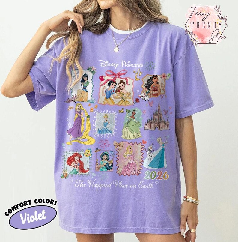 May include: A violet Comfort Colors t-shirt featuring Disney Princesses in framed illustrations. The shirt has the text "Disney Princess", "2026", and "The Happiest Place on Earth". The shirt is a relaxed fit.
