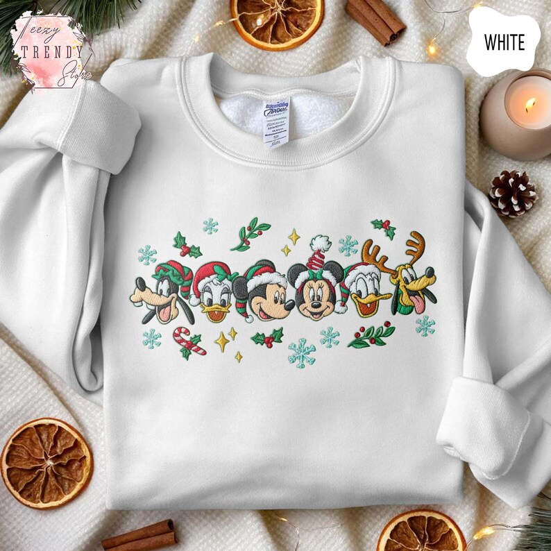 May include: White sweatshirt featuring embroidered Disney characters in Christmas attire. The design includes Mickey Mouse, Minnie Mouse, Donald Duck, Goofy, and Pluto, with snowflakes and candy canes. The sweatshirt has a crew neck and long sleeves.