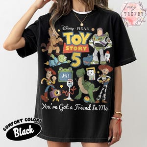 May include: A black short-sleeve t-shirt featuring a graphic print of Disney Pixar Toy Story 5 characters including Woody, Buzz Lightyear, Jessie, Rex, and Forky. The text reads Toy Story 5 and You've Got a Friend In Me with a small Hi sign.