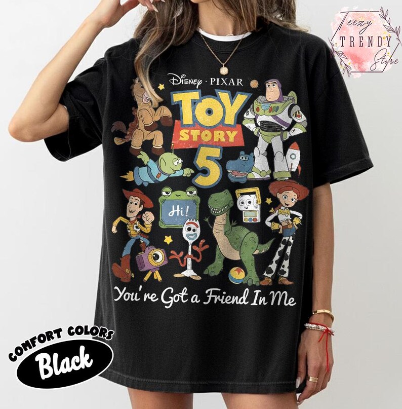May include: A black short-sleeve t-shirt featuring a graphic print of Disney Pixar Toy Story 5 characters including Woody, Buzz Lightyear, Jessie, Rex, and Forky. The text reads Toy Story 5 and You've Got a Friend In Me with a small Hi sign.