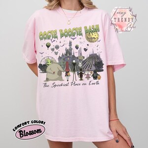 May include: A light pink t-shirt featuring a graphic print with the text OOGIE BOOGIE BASH and The Spookiest Place on Earth. The design includes characters from The Nightmare Before Christmas standing before a castle, a moon, and fireworks.