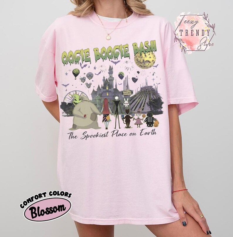 May include: A light pink t-shirt featuring a graphic print with the text OOGIE BOOGIE BASH and The Spookiest Place on Earth. The design includes characters from The Nightmare Before Christmas standing before a castle, a moon, and fireworks.