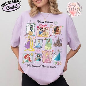 May include: A light purple t-shirt featuring Disney Princesses in framed illustrations. The shirt includes the text "Disney Princess" and "The Happiest Place on Earth" with the year "2026". The shirt is labeled "Comfort Colors" and "Orchid".