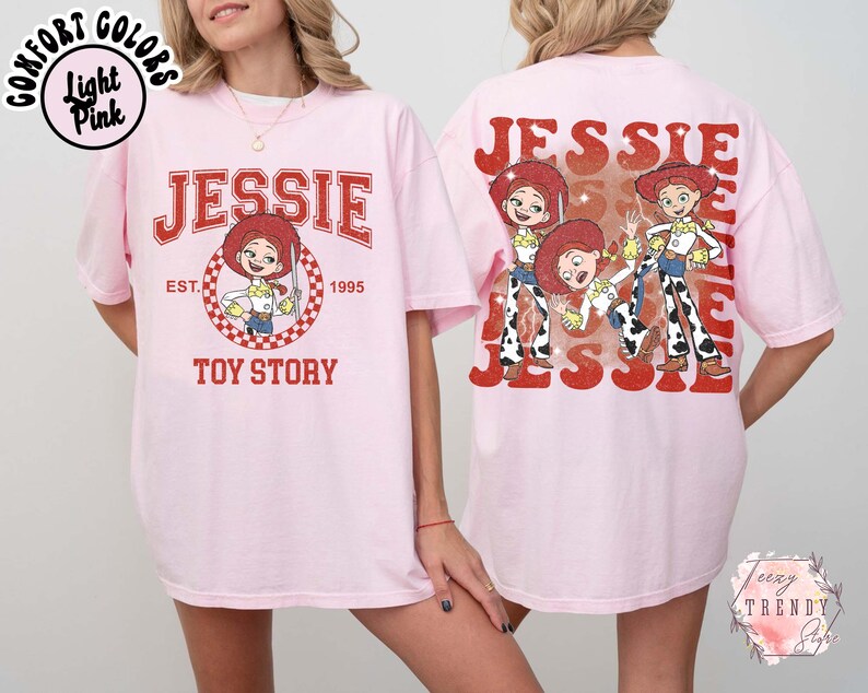 May include: Light pink t-shirt featuring Jessie from Toy Story. The front design includes the name "JESSIE" in red, a cartoon image of Jessie, and the text "TOY STORY EST. 1995". The back of the shirt displays multiple images of Jessie with the name "JESSIE".